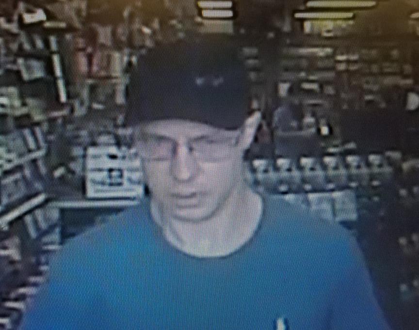 Surveillance image from Gamestop of suspect wearing dark colored ball cap, glasses and blue shirt.